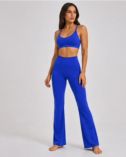 A woman modeling a bright royal blue activewear set consisting of a sports bra and high-waisted flared leggings, standing against a light gray studio background.