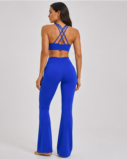 A woman is shown from the back wearing a bright royal blue two-piece activewear set consisting of a strappy halter crop top and matching high-waisted flared leggings, set against a plain light gray studio background.